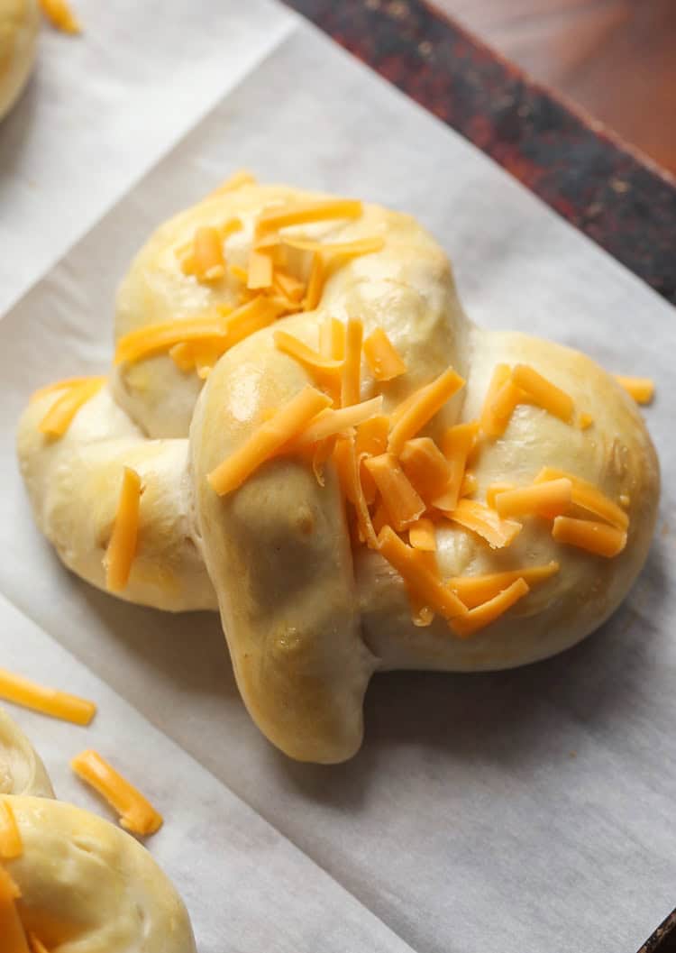 Shredded cheese is sprinkled over a wrapped "cracked out" soft pretzel prior to baking.