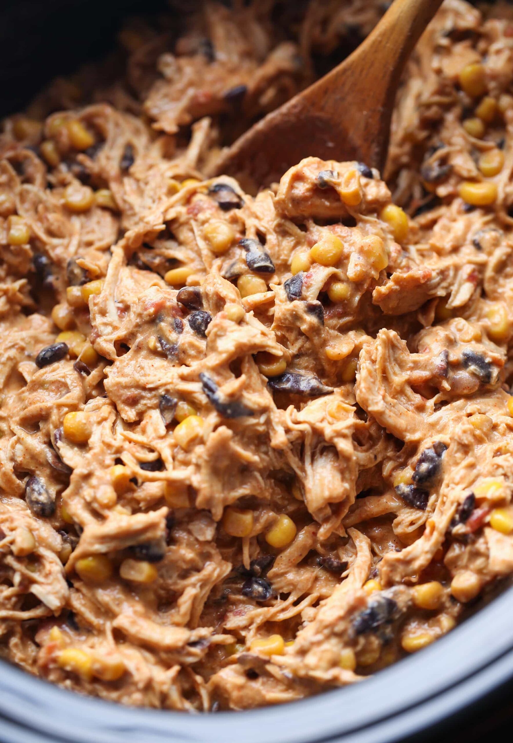 A Slow Cooker Full of Creamy Fiesta Chicken Being Stirred with a Wooden Spoon