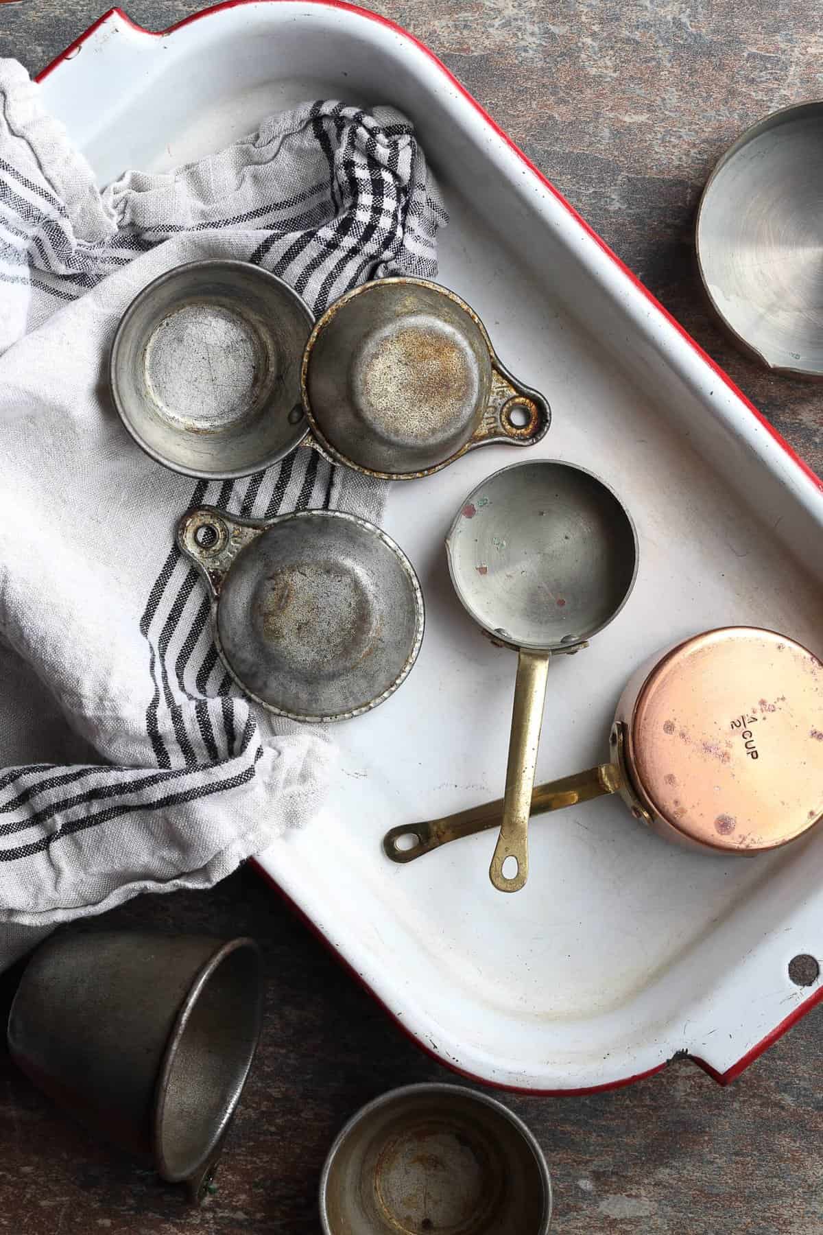 Assorted measuring cups scattered in a ceramic baking dish with a blue striped cloth.