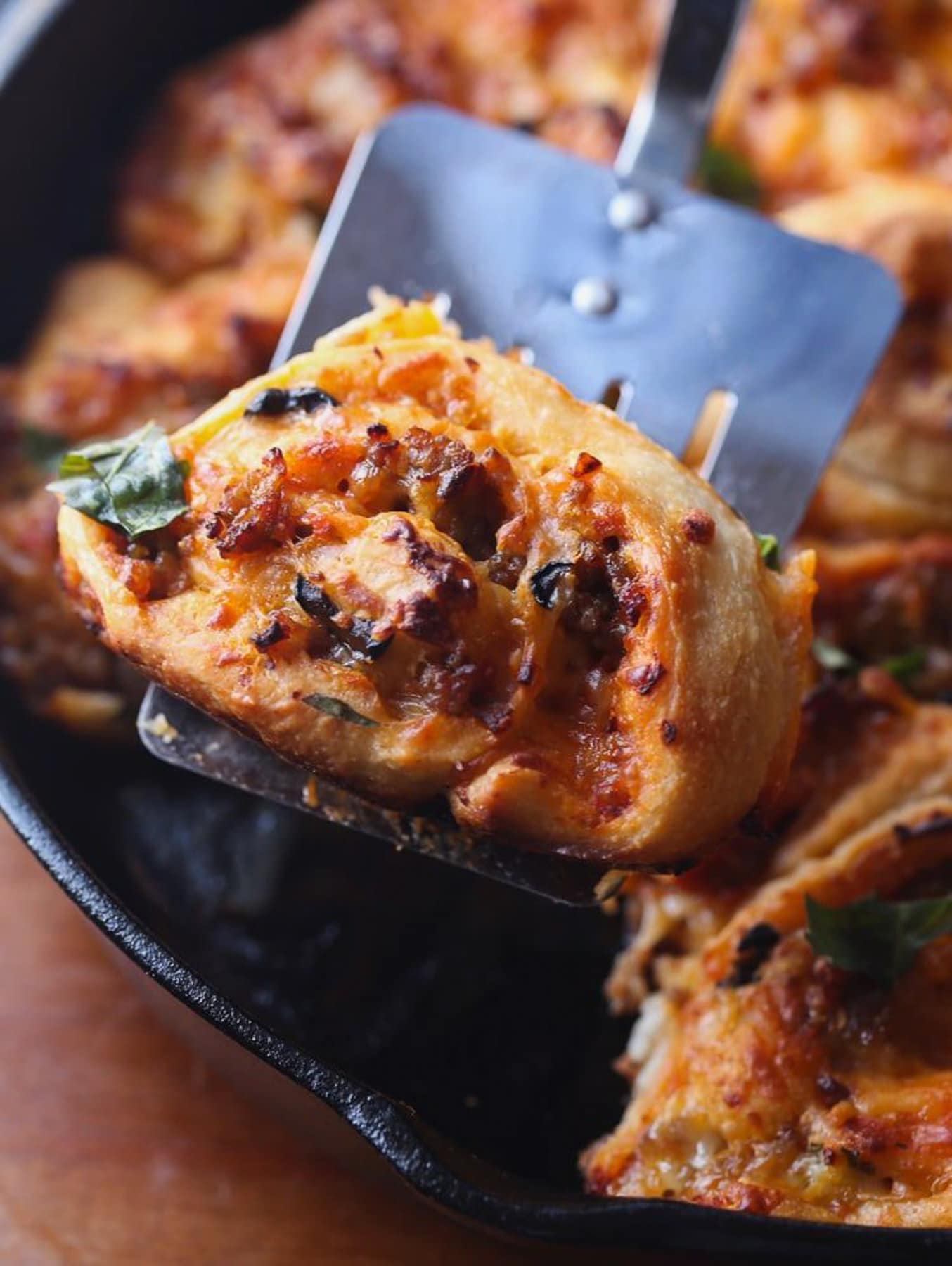 Skillet pizza rolls lifted out of a skillet with a spatula 