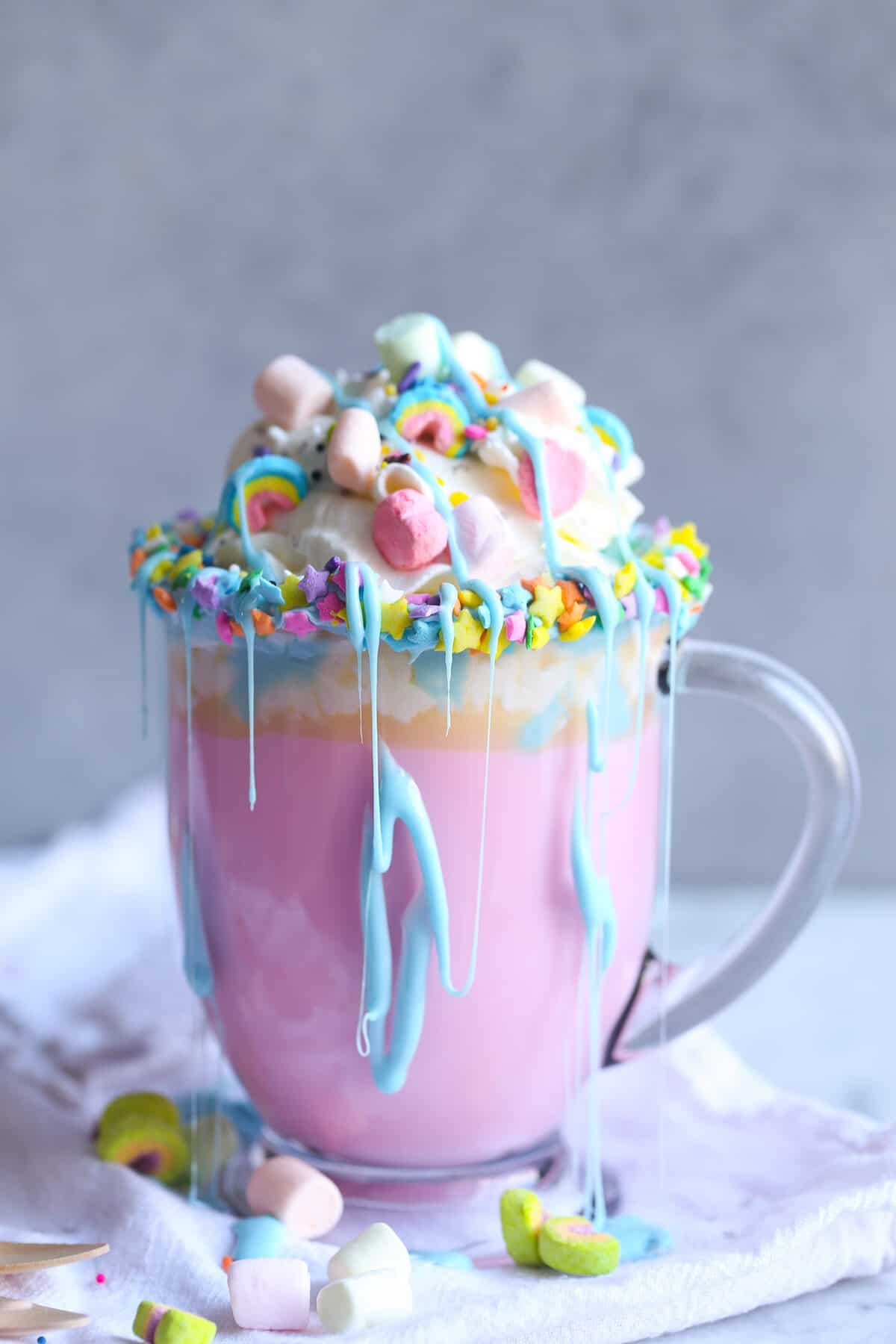 Unicorn Hot Chocolate! It's a creamy hot white chocolate, colored pink, topped with sprinkles, whipped cream, marshmallows, and a blue frosting drizzle!