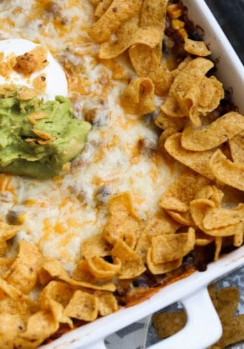 Overhead view of Frito pie in a 9x13 baking dish, topped with dollops of sour cream and guacamole.