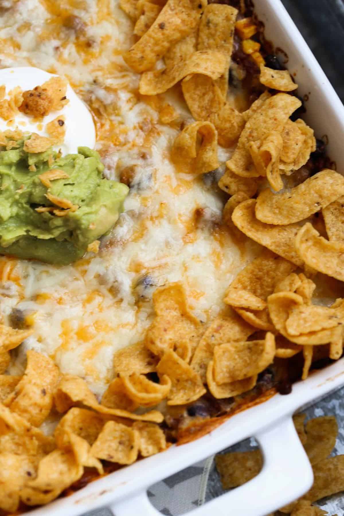 Overhead view of Frito pie in a 9x13 baking dish, topped with dollops of sour cream and guacamole.
