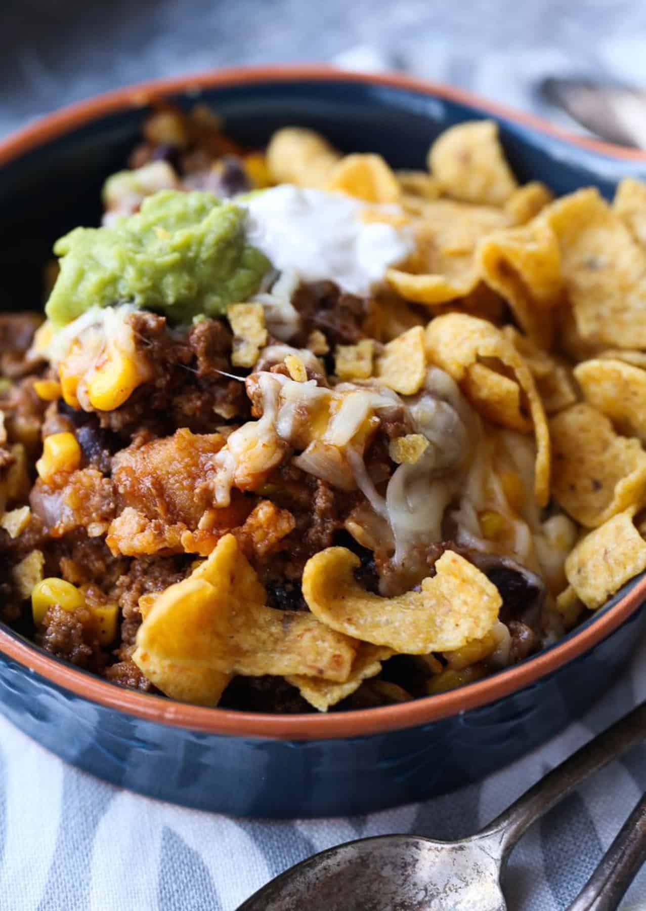 Frito pie served in a bowl topped with guacamole and sour cream.