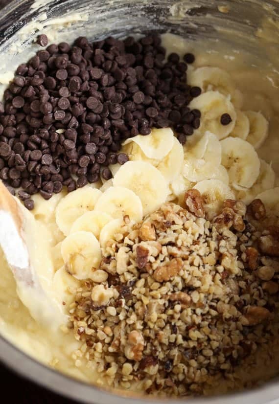 Chocolate chips, walnuts and sliced bananas on top of batter in a bowl.