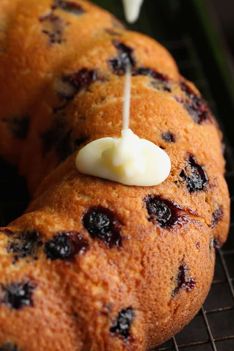 Pouring vanilla icing over a freshly baked blueberry bundt cake.