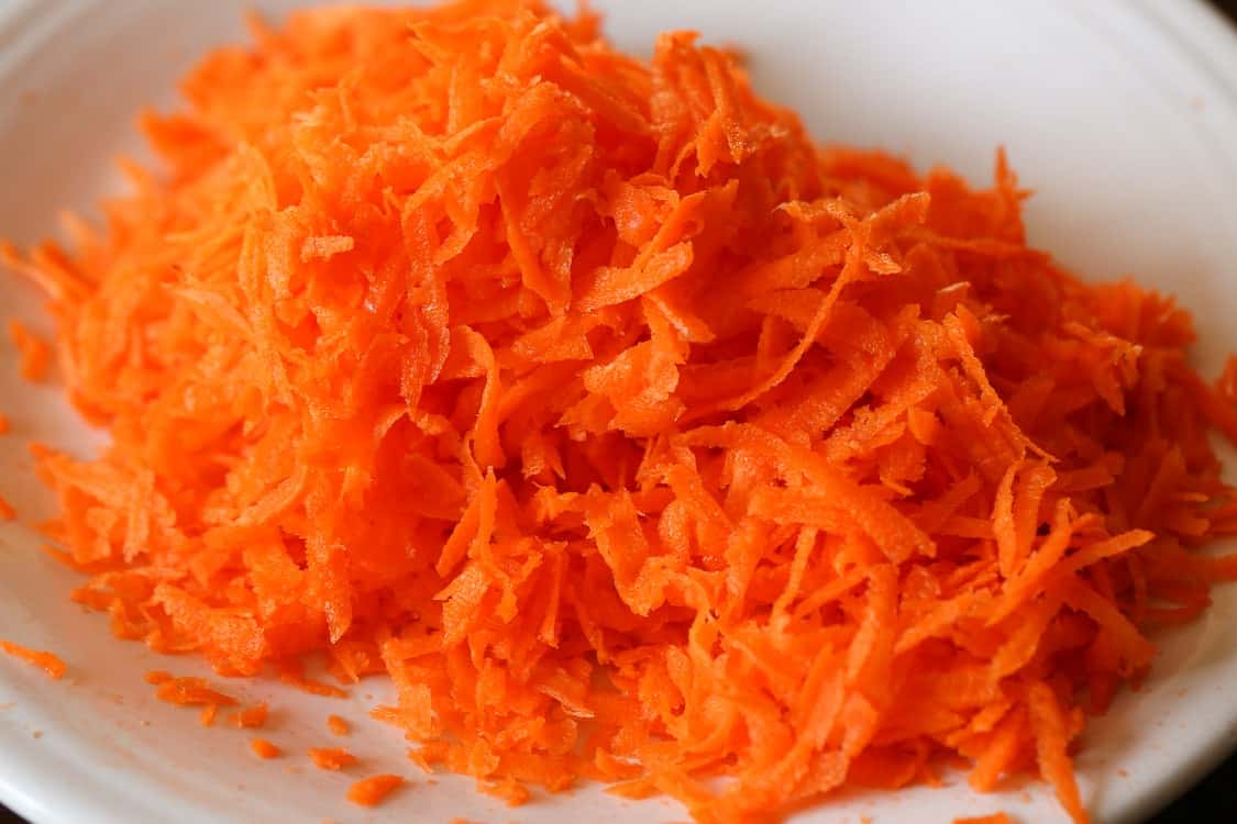 The best carrot cake recipe ever! Layers of moist cake filled with carrots, pineapple, and coconut, covered with rich cream cheese frosting. Shredded carrots in a bowl.