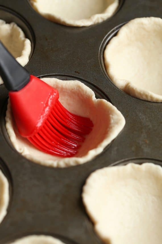 brushing garlic butter onto dough in muffin tin