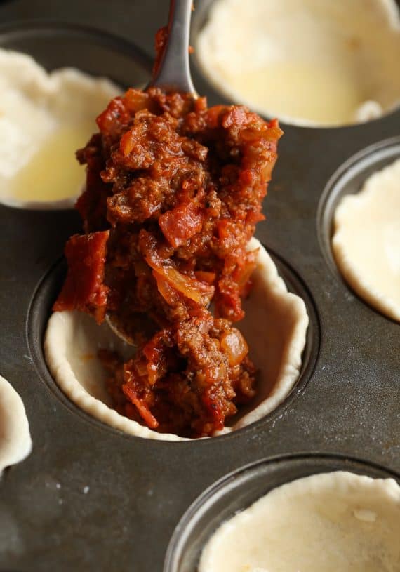 spooning meat sauce into dough in a muffin tin