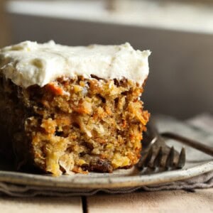 A perfectly moist and fluffy slice of frosted carrot cake on a plate next to a fork