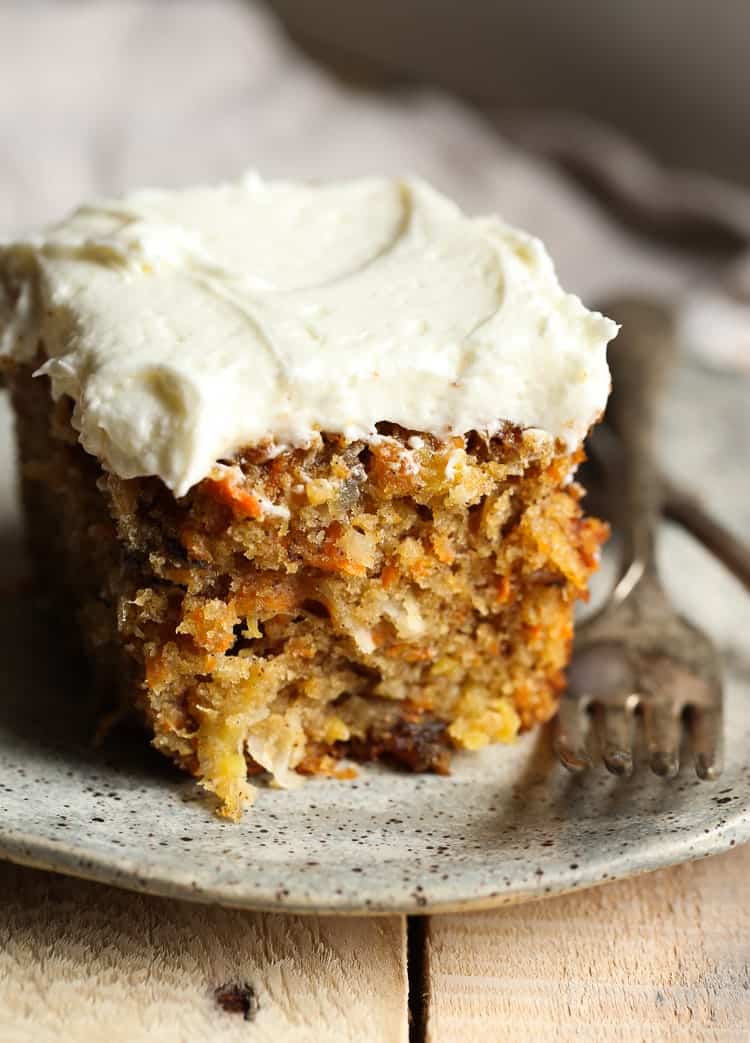 A slice of fluffy, tender carrot cake topped with cream cheese frosting, on a plate