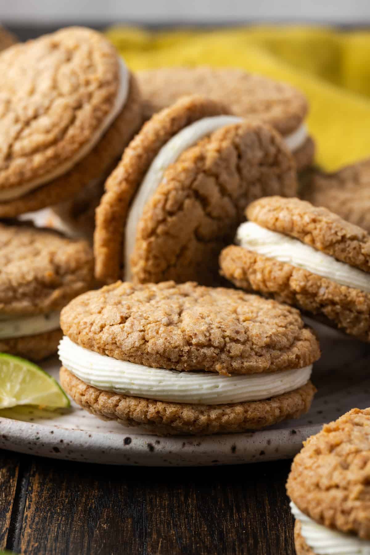 These key lime sandwich cookies taste like the classic pie, with two soft, chewy graham cookies filled with zesty key lime buttercream. Close up of assorted key lime sandwich cookies piled on a plate.