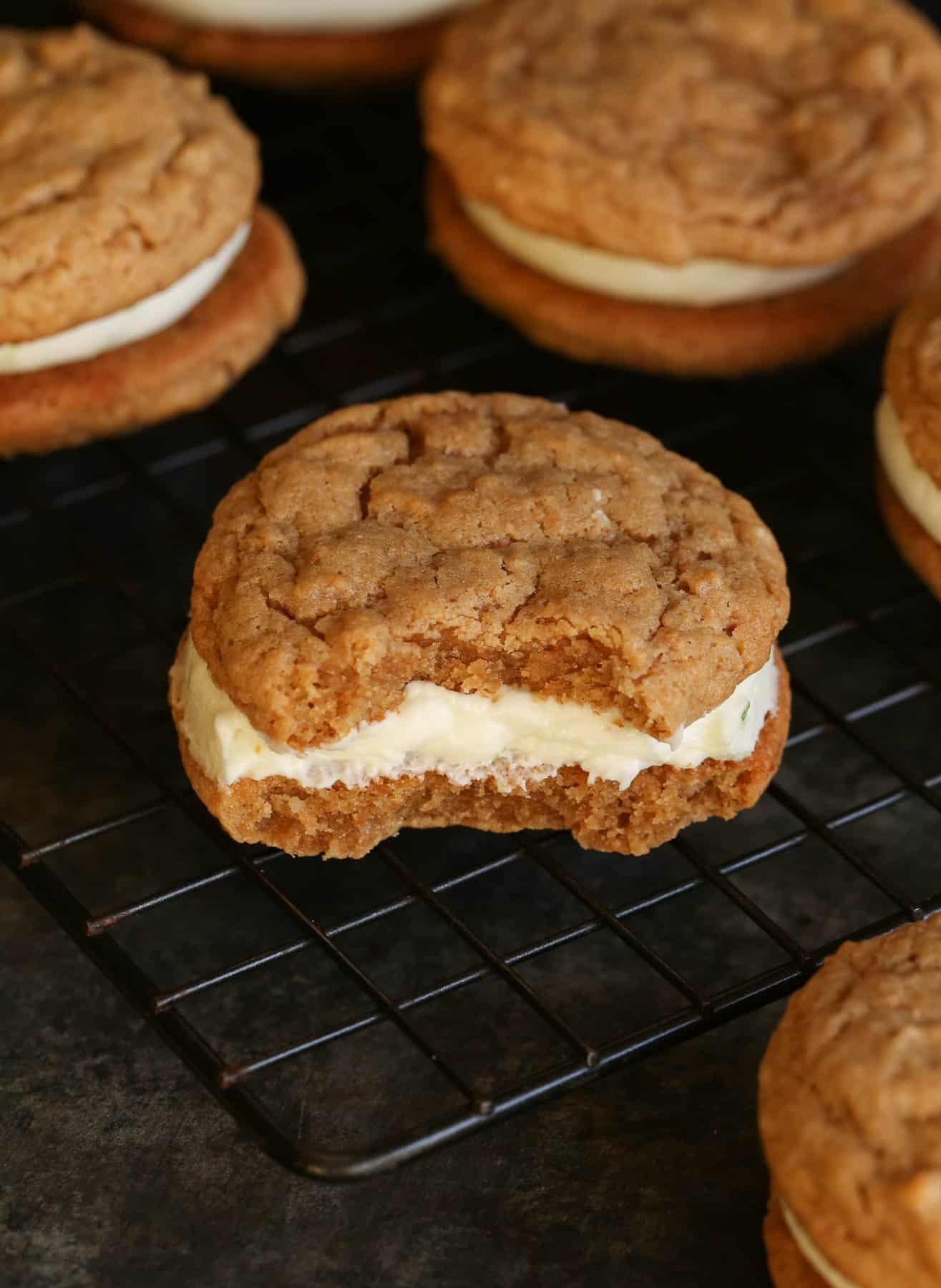 Key Lime Pie Sandwich Cookies on a wire rack, with a bite missing from one cookie.