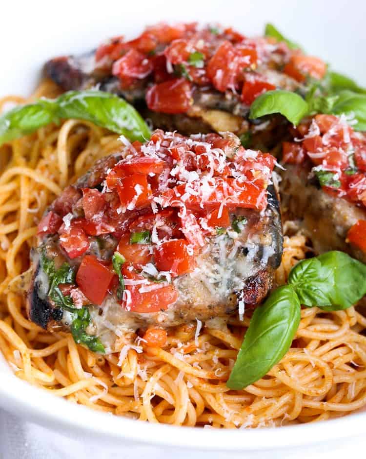 Grilled bruschetta chicken served over a bed of spaghetti, garnished with basil.