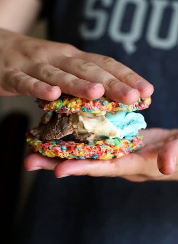 Two hands pressing a Fruity Pebble Ice Cream Sandwich together