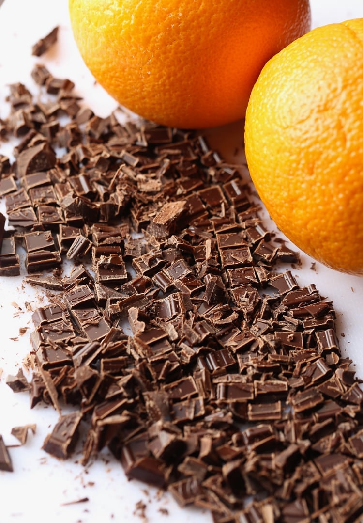 Chopped Chocolate on a White Surface Next to Two Fresh Oranges