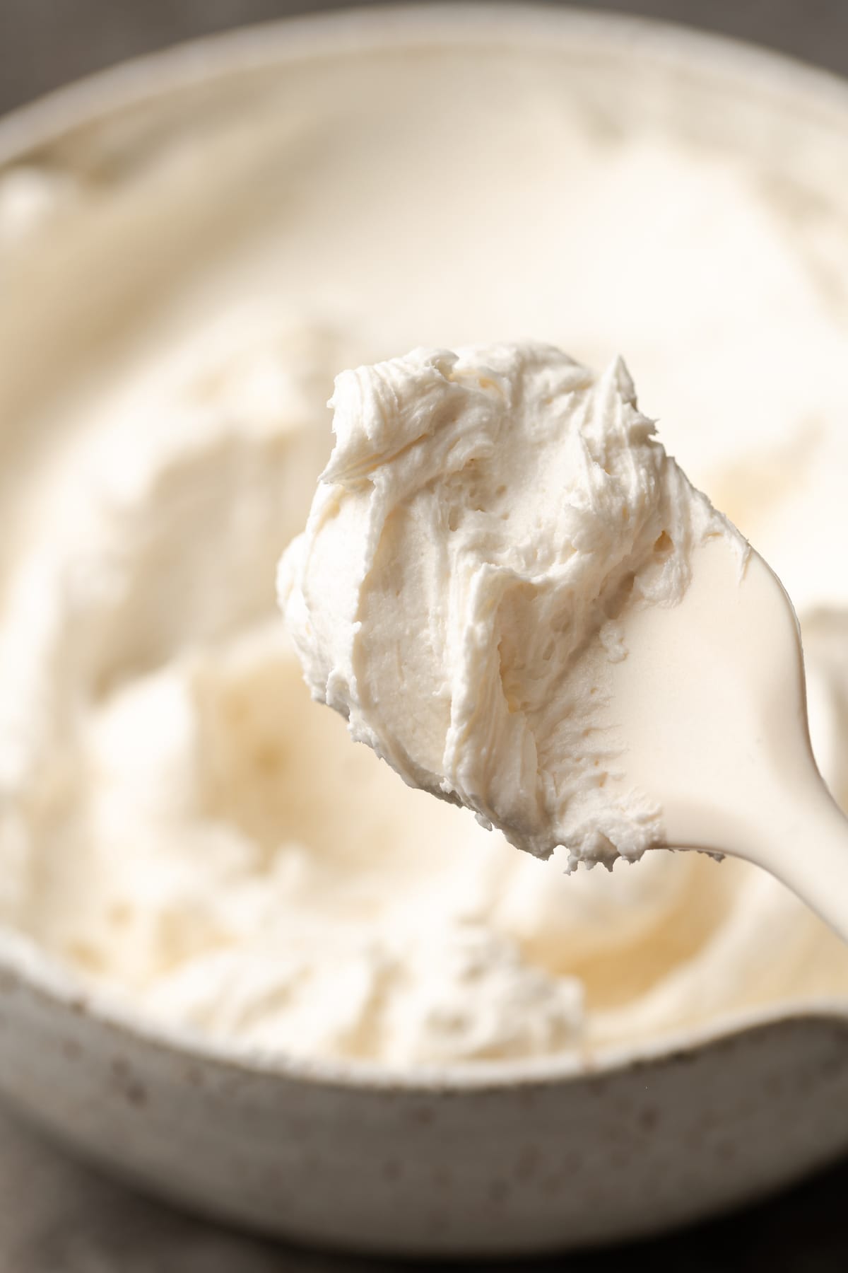 A spoon with a scoop of vanilla buttercream held over a bowl of frosting.