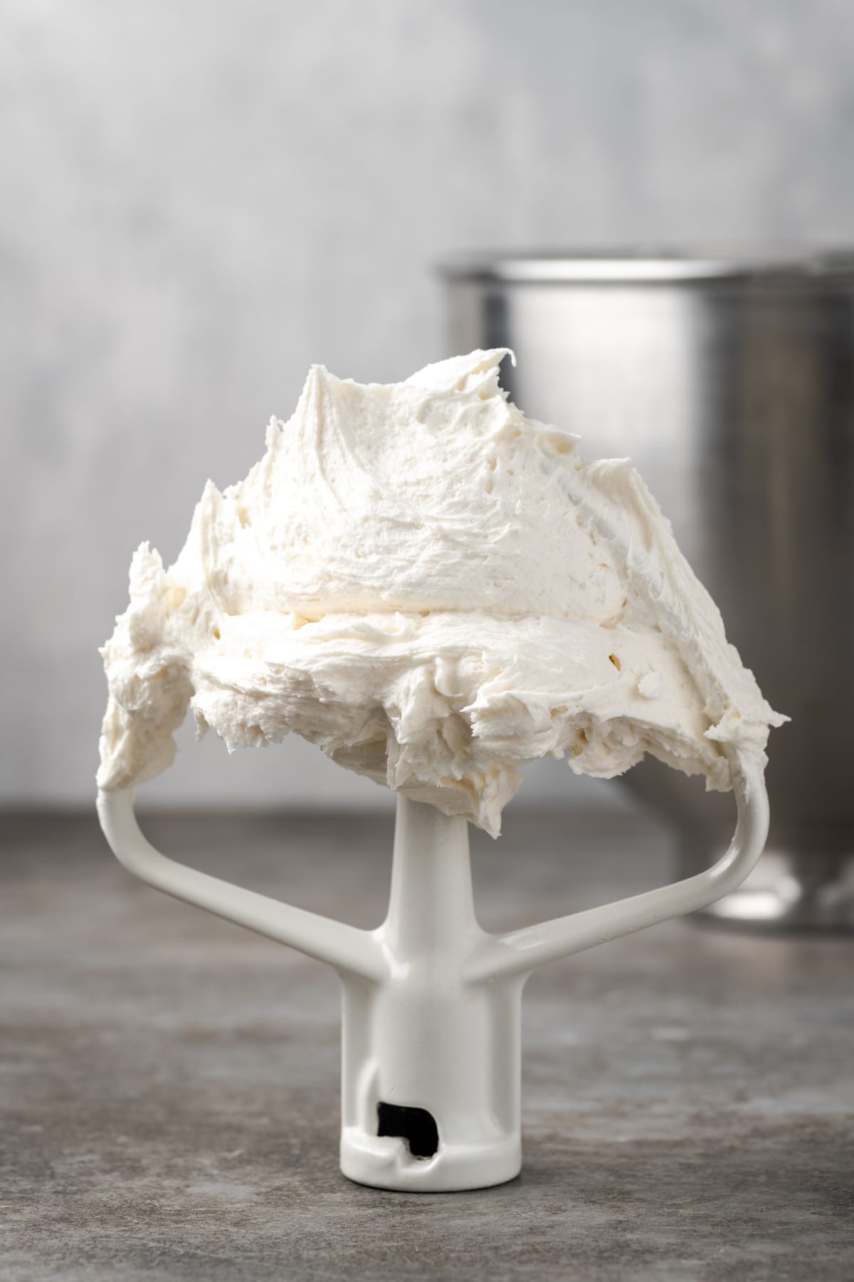 Vanilla buttercream frosting on a stand mixer attachment, propped upright on a countertop.