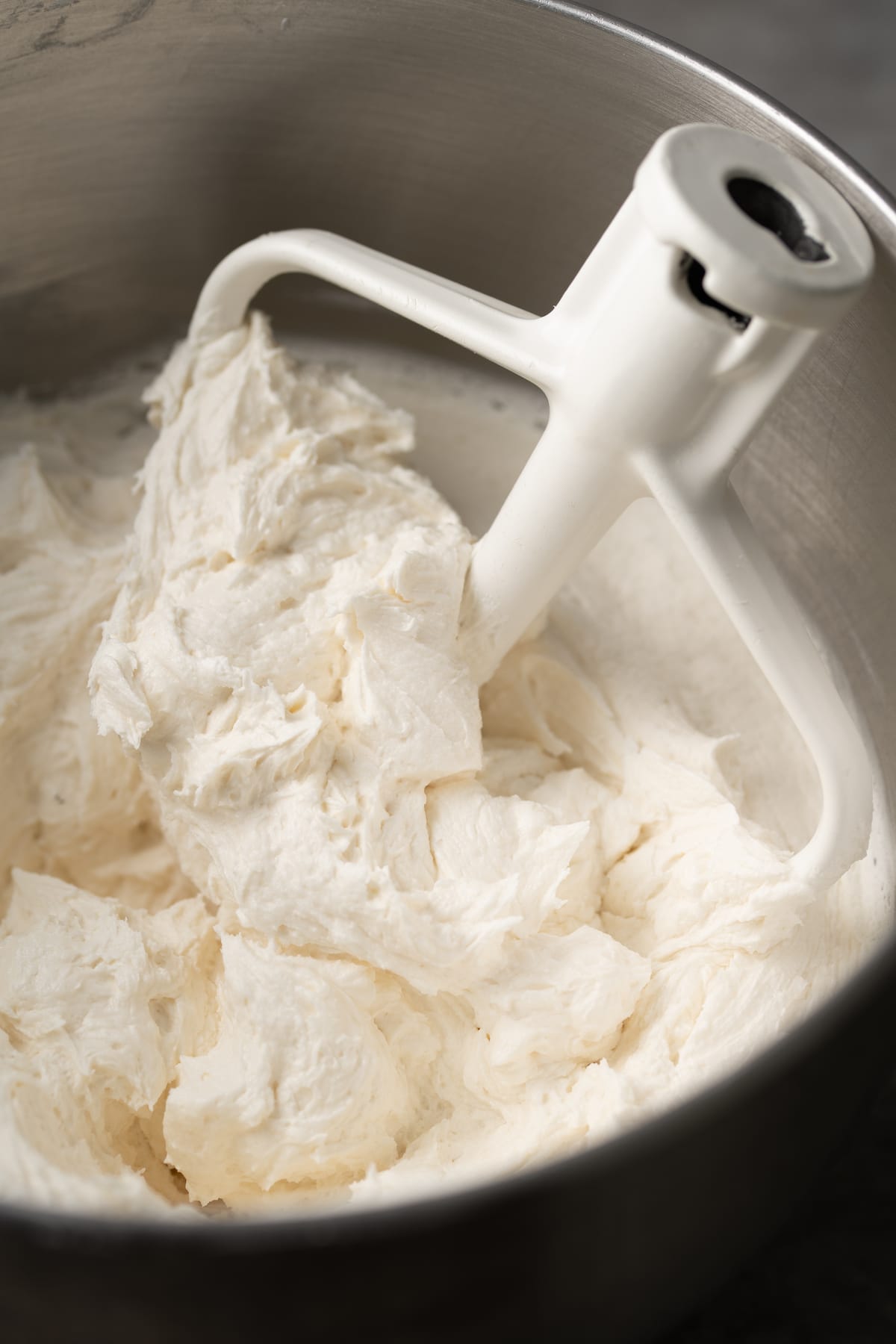 A stand mixer attachment stuck into a bowl of perfect buttercream frosting.
