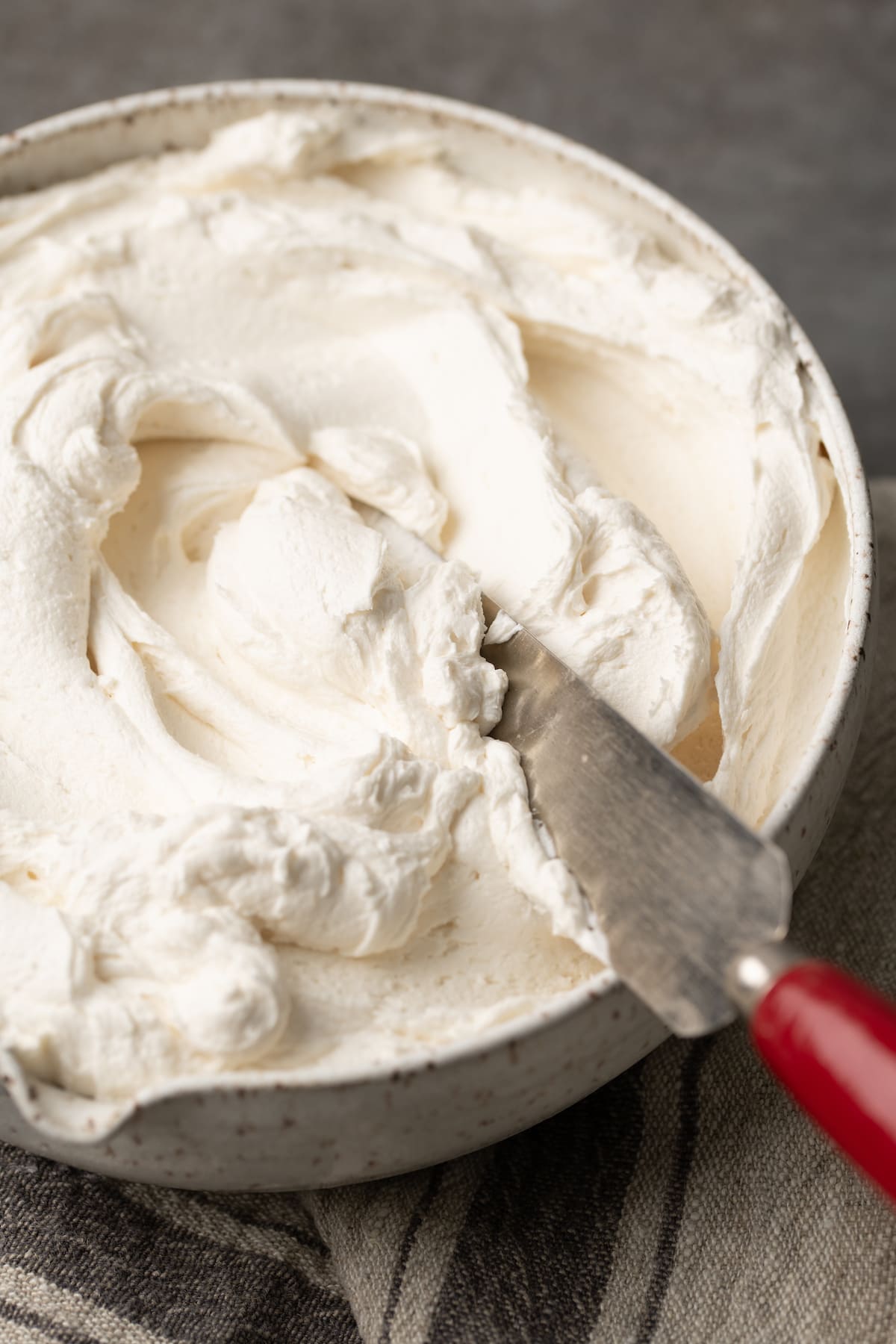 An offset spatula stuck into a bowl of buttercream frosting.