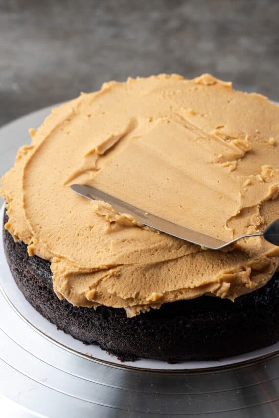 An offset spatula being used to spread peanut butter filling over the first chocolate cake layer.