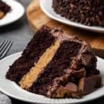 A slice of Reese's cake on a white plate with the rest of the cake in the background.