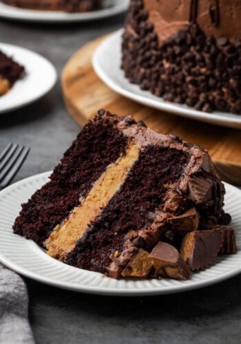 A slice of Reese's cake on a white plate with the rest of the cake in the background.