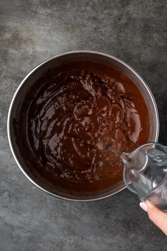 Warm water being added to chocolate cake batter in a mixing bowl.