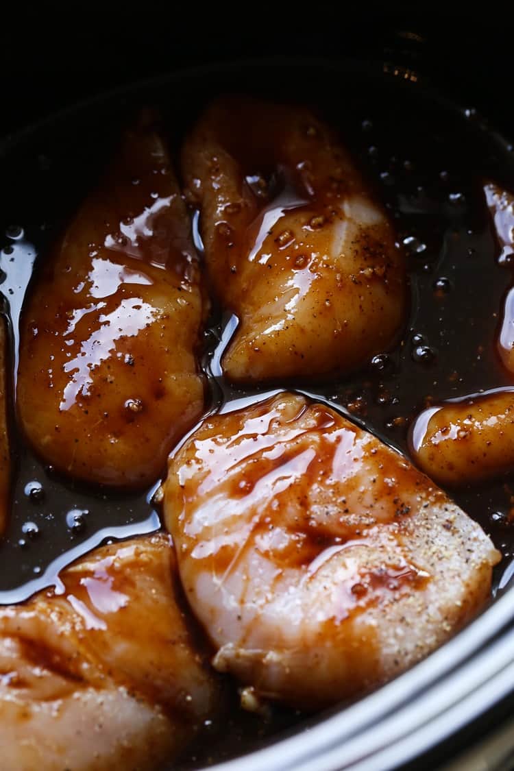 Chicken breasts and honey garlic sauce in the bowl of a slow cooker.