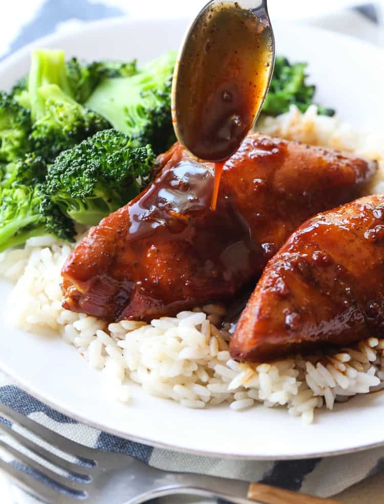 Sauce is drizzled over honey garlic chicken served on a bed of rice with broccoli.