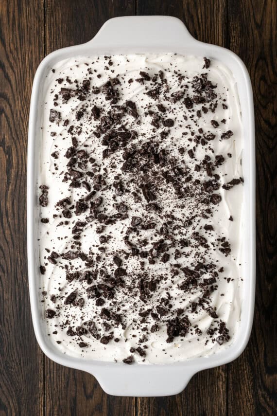 Assembled chocolate lasagna topped with whipped cream and crushed Oreos in a casserole dish.