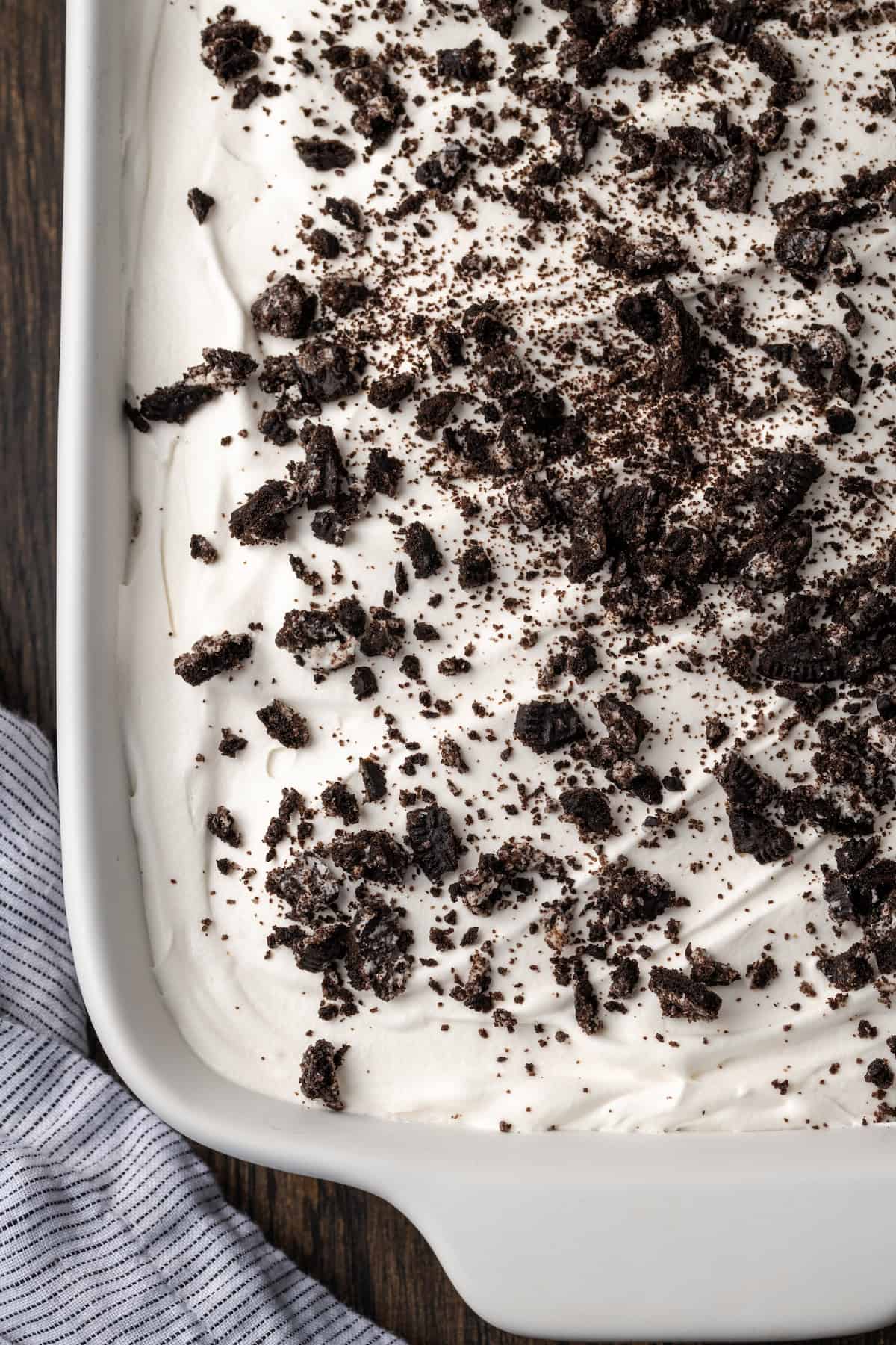 Close up view of chocolate lasagna topped with whipped cream and crushed Oreos in a casserole dish.