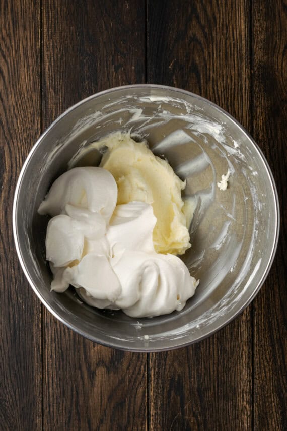 Whipped topping added to creamed cream cheese and sugar in a metal bowl.