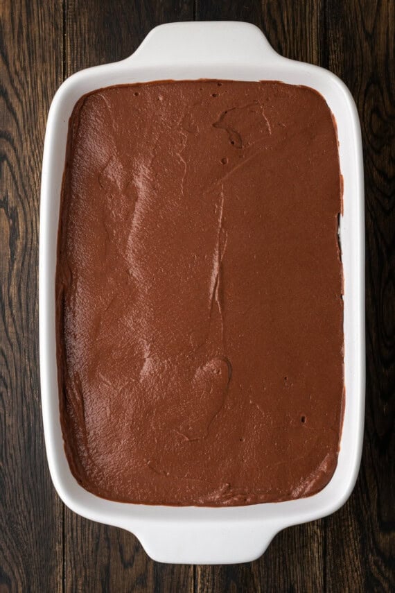 Chocolate pudding layer added over top of the cream cheese layer and Oreo crust in a ceramic baking dish.