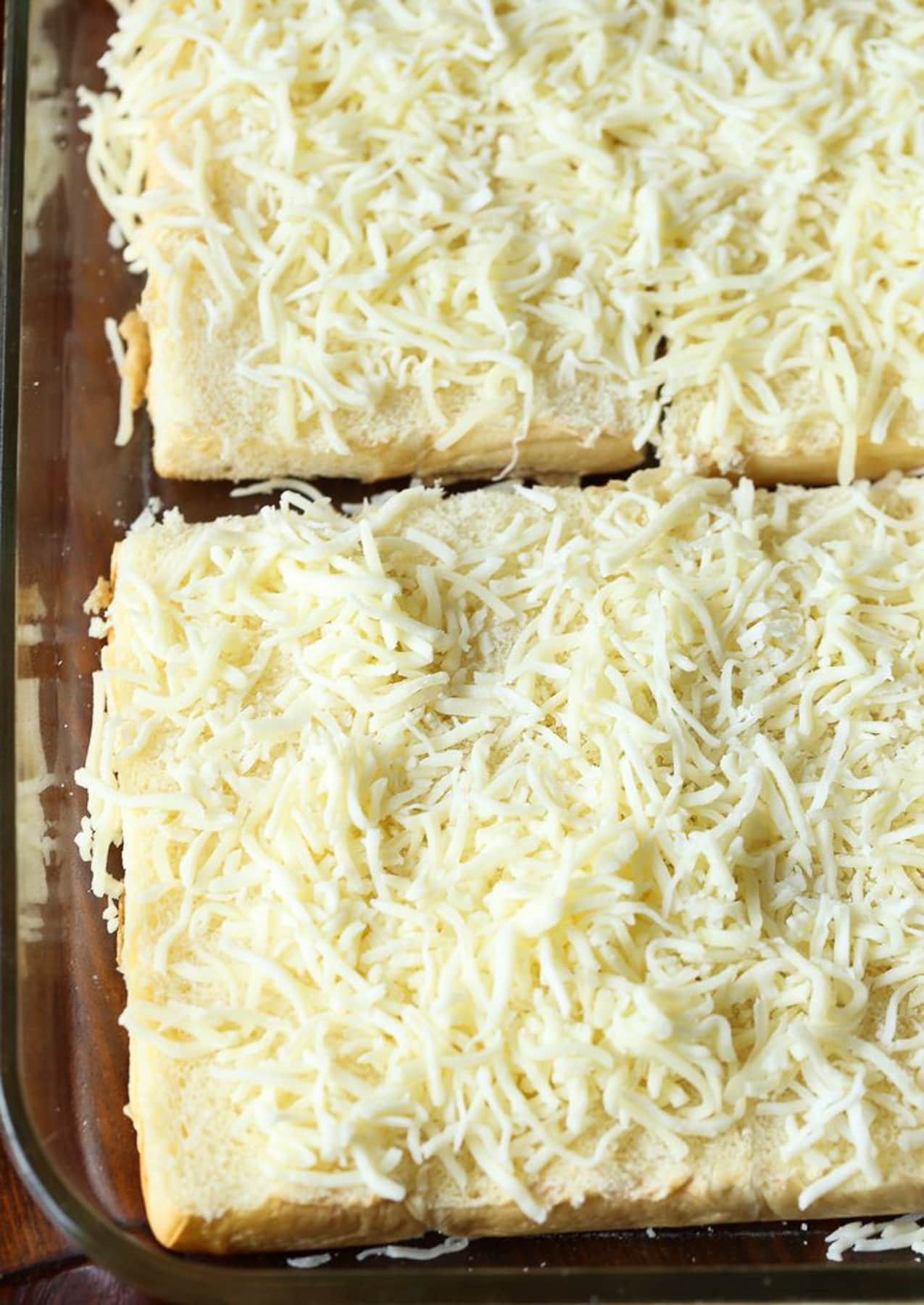 These cheesy chicken parmesan sliders are the best party food! An easy game day appetizer or kid-friendly dinner that's ready in 30 minutes. The bottoms of Hawaiian rolls topped with shredded cheese.