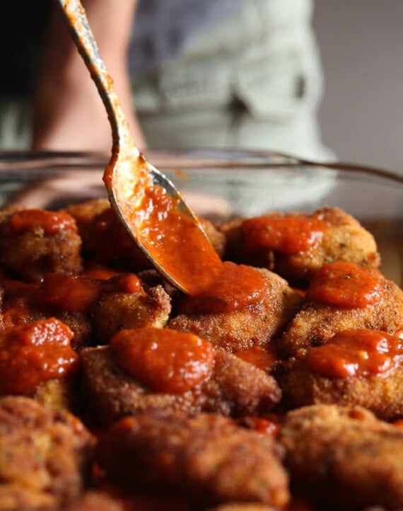 These cheesy chicken parmesan sliders are the best party food! An easy game day appetizer or kid-friendly dinner that's ready in 30 minutes. A spoon dropping marinara sauce on top of chicken on slider buns.