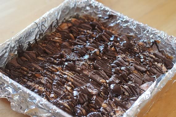 Chocolate drizzled over caramel and marshmallows in a foil-lined pan