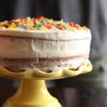 Side view of a cake on a yellow cake stand with Cereal Milk Frosting and colorful cereal pieces on top
