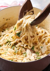 Tongs are used to lift crab alfredo pasta from a large pot.