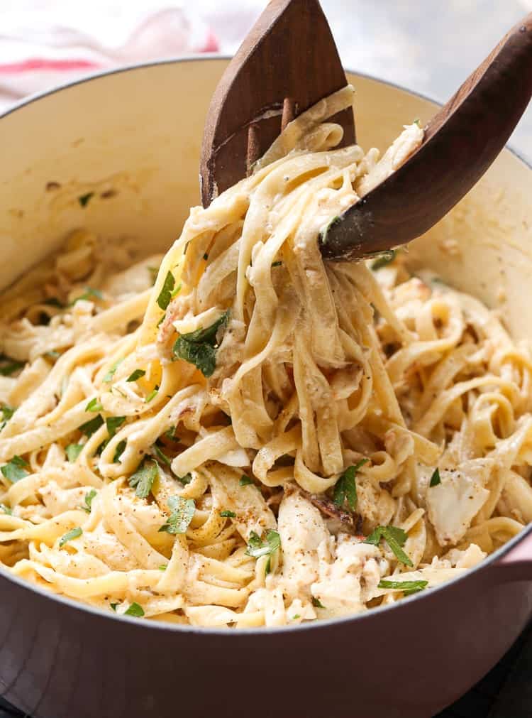 Tongs are used to lift crab alfredo pasta from a large pot.