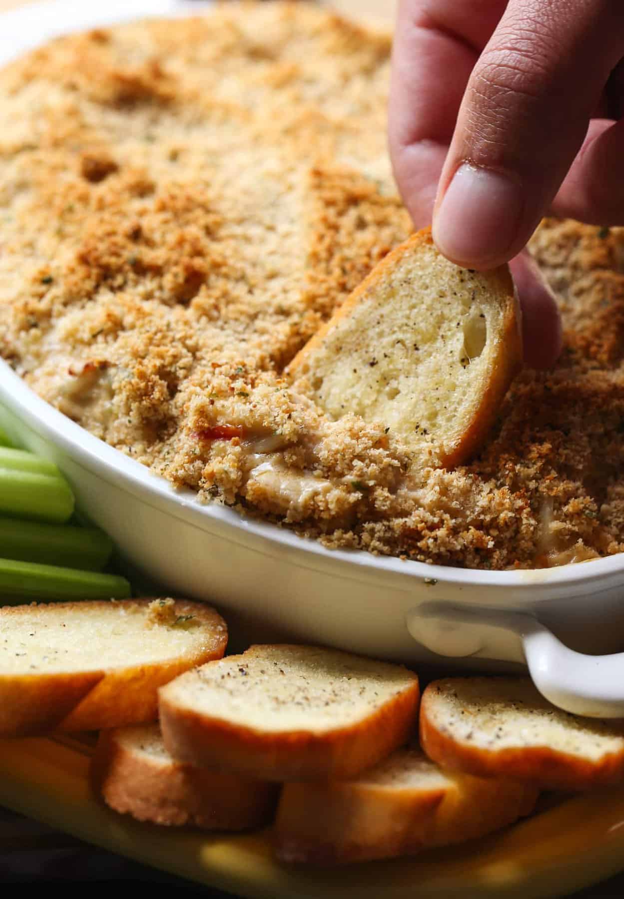 Baked crab dip is an easy appetizer packed with lump crab, cream cheese, and Old Bay seasoning. It's rich, creamy, and perfect on a cracker! A hand dipping a cracker into warm crab dip in a baking dish.