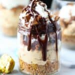 A no bake Butterfinger cheesecake cup loaded with Butterfinger candies and drizzled with chocolate sauce.