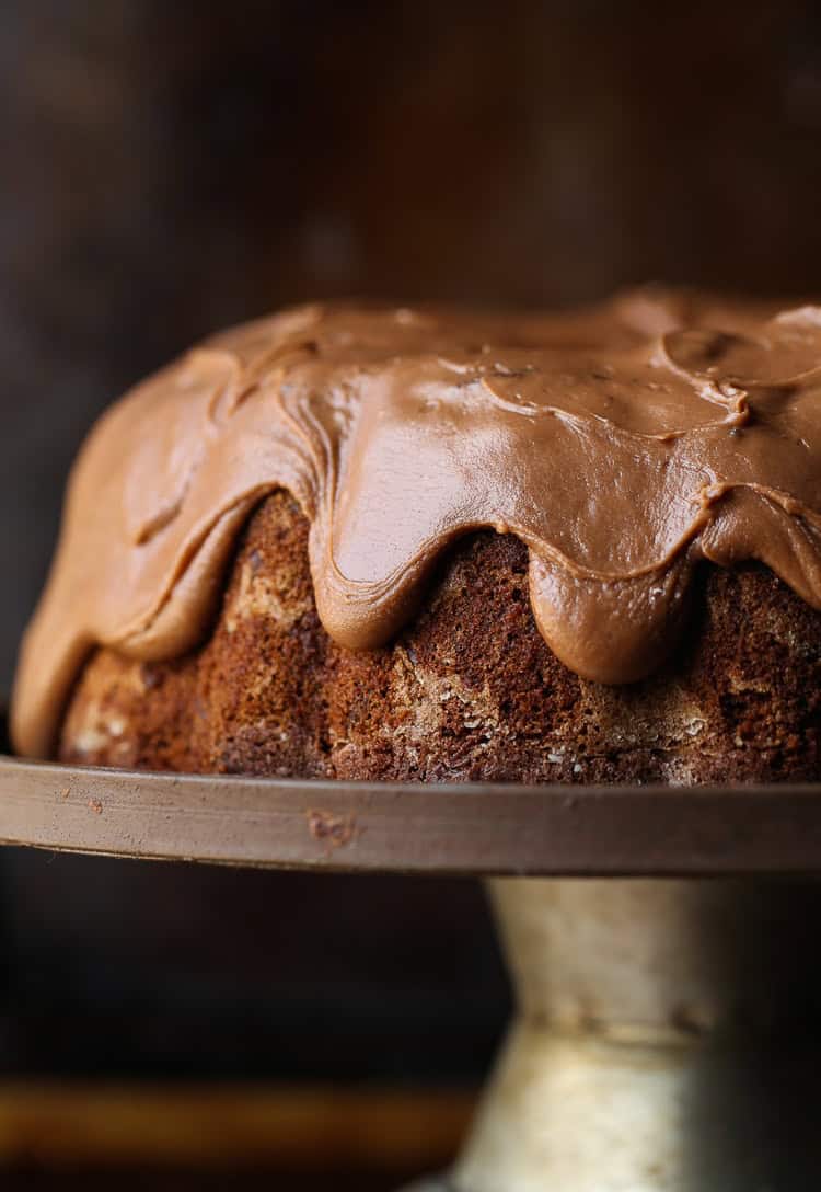 A frosted chocolate bundt cake on a metal cake stand