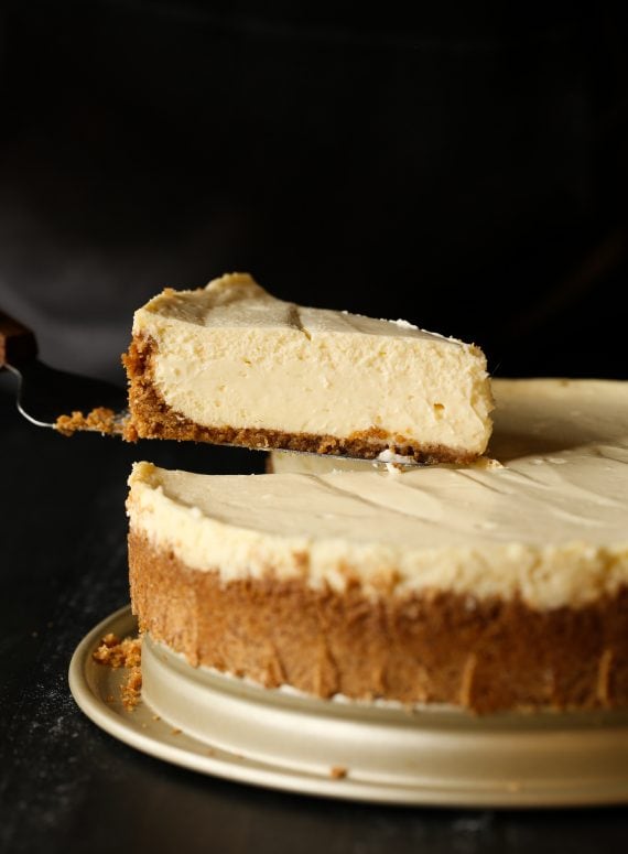 A slice of creamy cheesecake being lifted on a spatula.