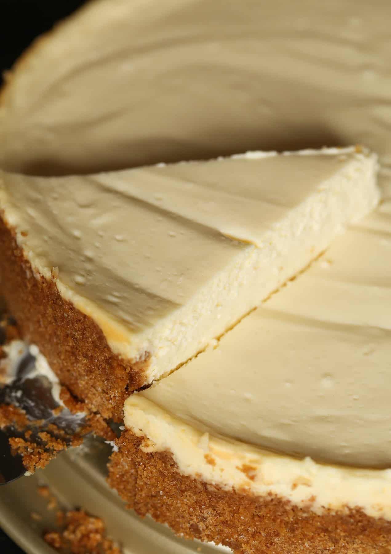 A close up of a slice of cheesecake being taken out of the whole cheesecake.