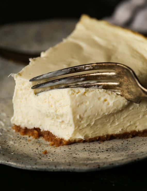 Close up of a fork cutting into a slice of cheesecake.