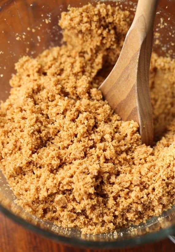 A wooden spoon stirring graham cracker crumbs and butter