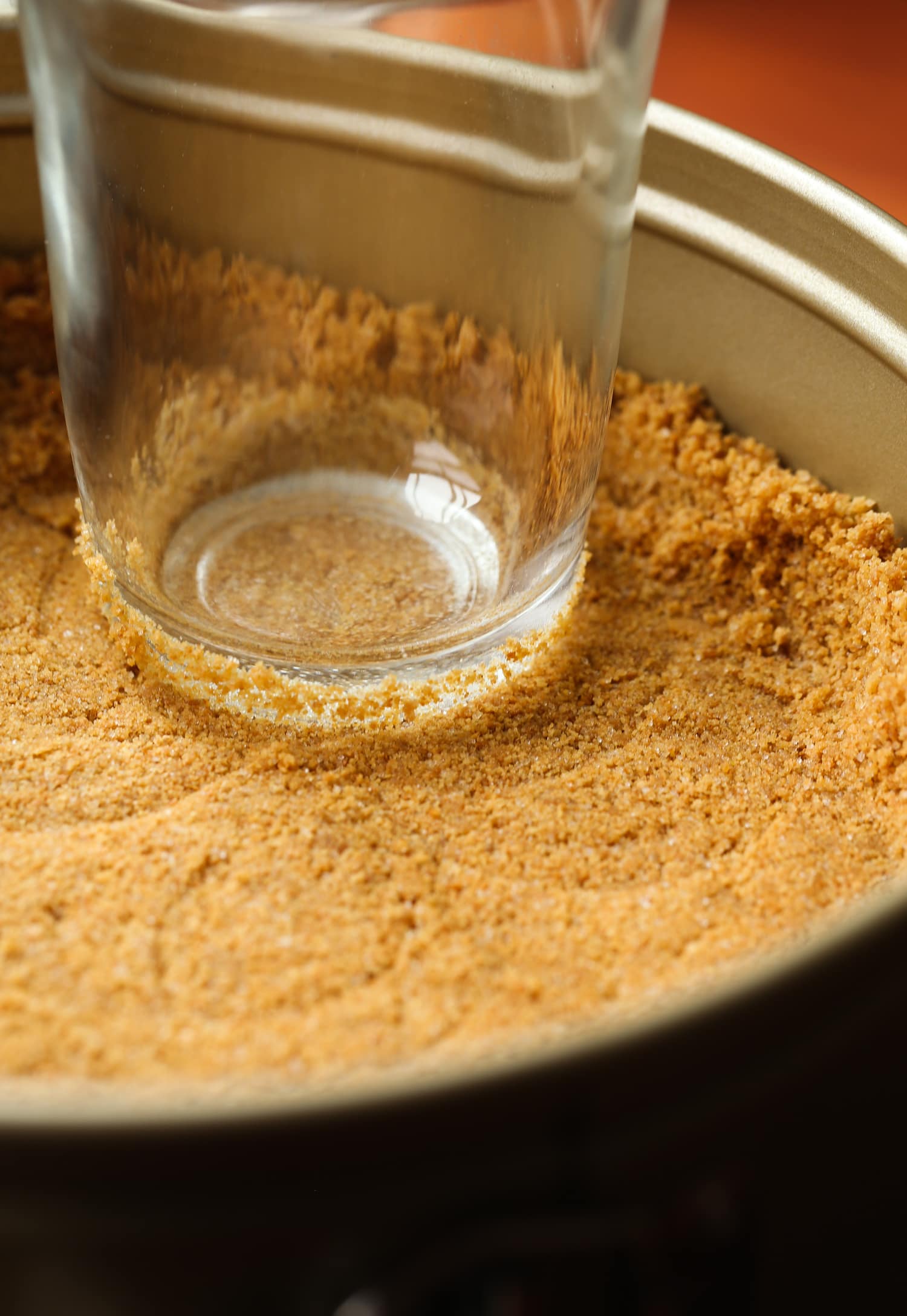 A springform pan with graham cracker crust being shaped with a cup.