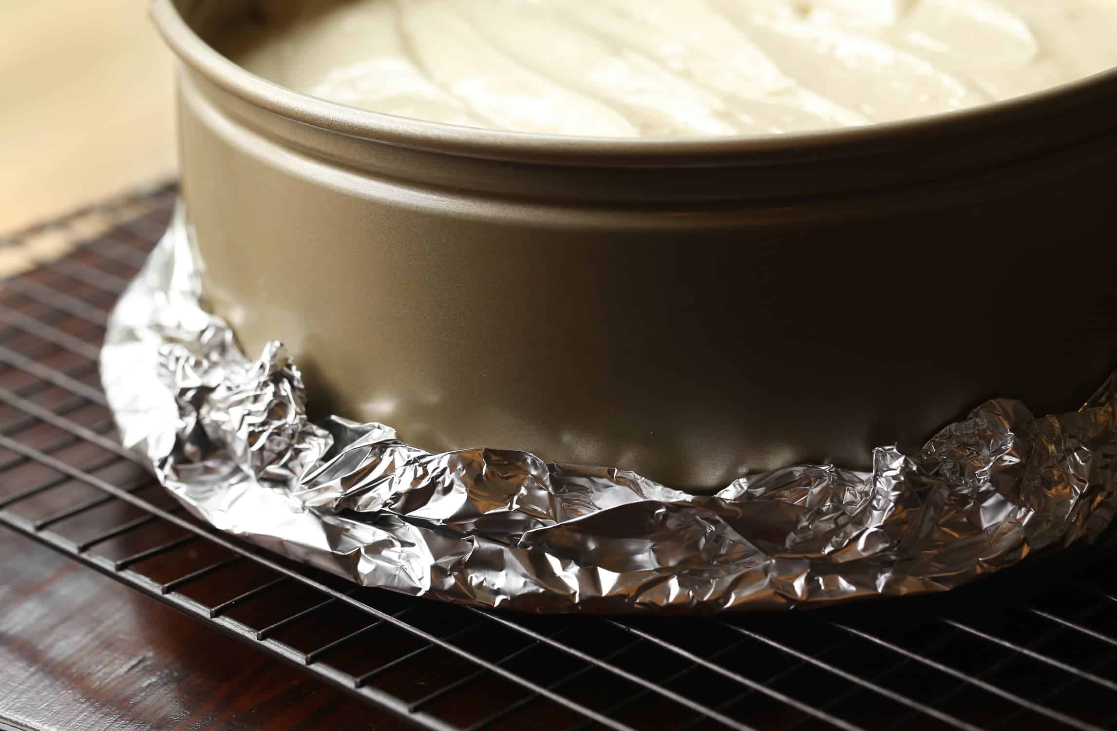 Cheesecake in a springform pan wrapped with tin foil.