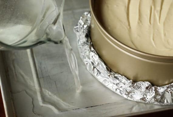 A tin foil wrapped springform pan in a baking sheet with hot water.